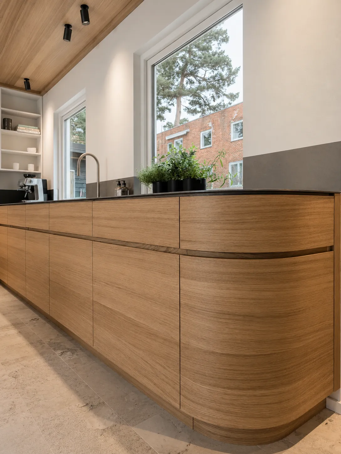 Prosjekt 01 — Et moderne kjøkken med fronter i varmt tre, et avrundet benkehjørne og en elegant, tynn benkeplate i rustfritt stål.